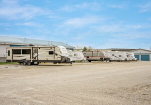 AllSeason_021a Row of travel trailers and campers parked in the outdoor RV storage lot on a clear blue day near Wind Lake and Waterford, WI