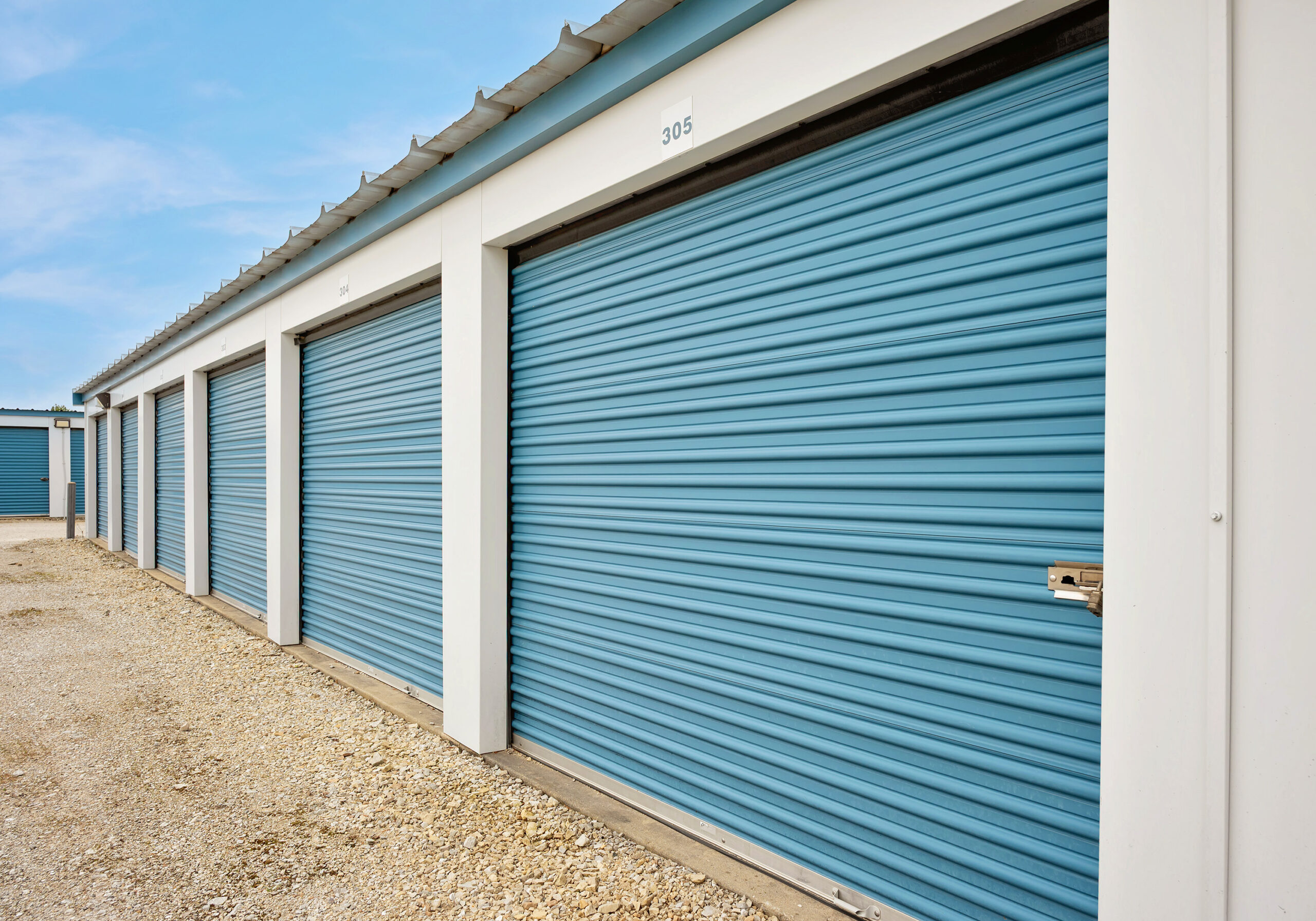 AllSeason_031a All Seasons Storage unit building with numbered roll-up doors and gravel drive aisle in Franksville, WI